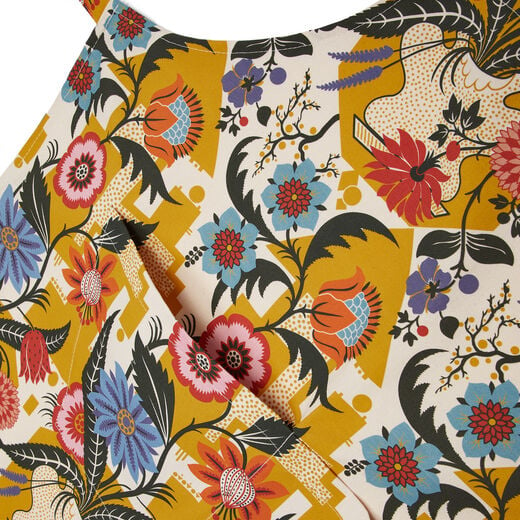 A detail of the front pocket of an apron. The textile features a pattern of blue, red and yellow flowers on white and yellow background.